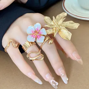 Dettaglio di eleganti anelli a fiore 3D dorati con smalto rosa sulla mano della modella