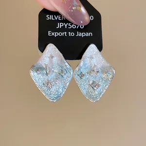 Primo piano di orecchini a rombo in argento testurizzato con pietre di zircone lucide.