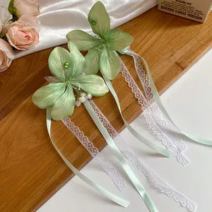 Détail des pinces à cheveux en fleurs de tissu vert clair avec rubans de dentelle élégants.