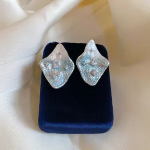 Primo piano di orecchini a rombo in argento con texture stropicciata e zirconi brillanti.