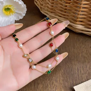 Detail view of layered gold necklace with colorful oval gems and white pearls.