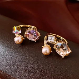 Macro view of elegant gold-plated open rings with oval crystal and pearl details.