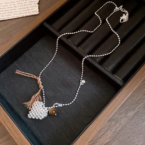 Detail shot of a minimalist beaded heart pendant necklace with a brown tassel accent