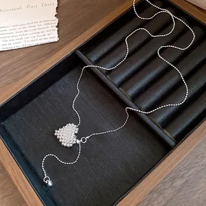 Close-up of minimalist silver woven heart pendant necklace on a jewelry tray.