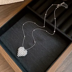 Close-up detail of a silver beaded woven heart pendant on a minimalist chain