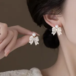 Close-up of French vintage hollow bow stud earrings with elegant pearls on model.
