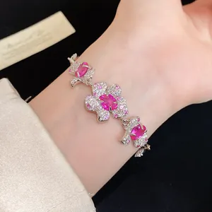 Nahaufnahme eines silbernen Armbands mit rosa Zirkonia-Blumenanhängern am Handgelenk.