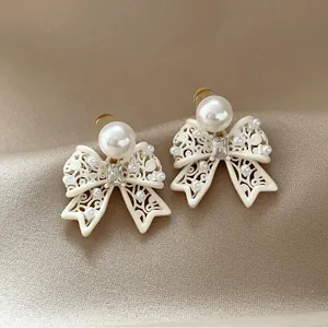Macro detail view of elegant French vintage pearl bow hollow stud earrings on beige fabric