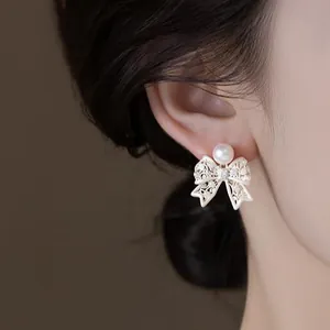 Close-up of white hollow lace bow earrings with a round pearl detail on ear