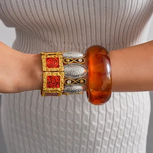 Dettaglio di bracciali vintage in metallo e bracciale rigido in resina ambra sul polso