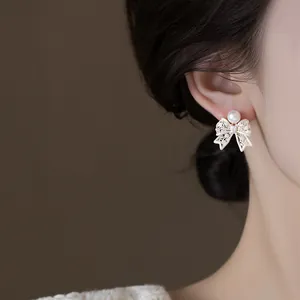 Close-up of French vintage pearl bow earring on model's ear, elegant and hollow design.