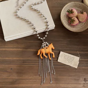 Detail view of a playful orange resin horse pendant with silver tassel on a bead chain