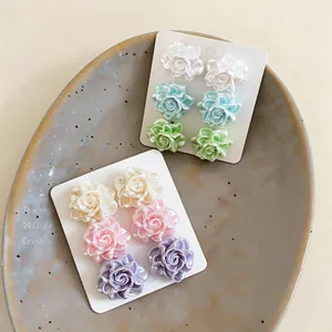 Primo piano di dolci orecchini a lobo a fiore in resina pastello, bianco e rosa.