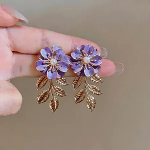 Elegante lila Emaille-Blumenohrringe mit goldenen Blattquasten und Perlenzentren.