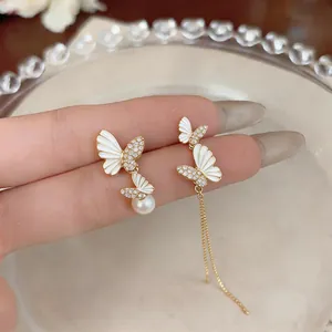 Detailed view of asymmetric butterfly earrings with white enamel and pearl drops