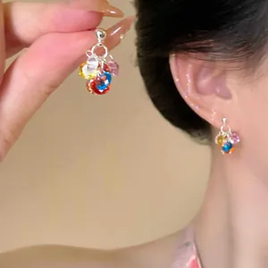 Vista detallada de pendientes de borla de cristal multicolor en la oreja y mano.