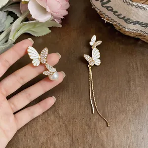 Detailed close-up of asymmetrical white enamel butterfly earrings with rhinestones