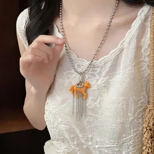 Close-up of a cute orange resin horse pendant necklace with metal tassels on a model.