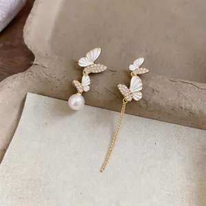 Close-up detail of gold-tone asymmetric butterfly earrings with white pearls and long chain