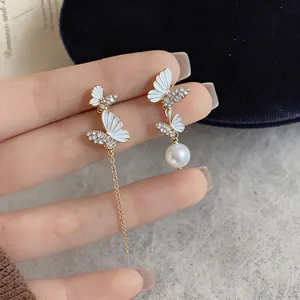 Detailed macro shot of asymmetrical butterfly earrings with white enamel and pearl drop