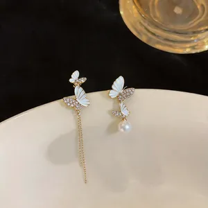 Detailed view of asymmetrical gold-toned butterfly earrings with white enamel and pearls.