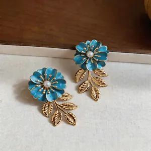 Detaillierte Ansicht eleganter blauer Emaille-Blumenohrringe mit Goldblättern und Perlen.