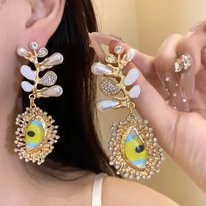 Close-up detail of ornate gold-tone branch earrings with pearls and blue-yellow eye charm