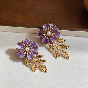 Detaillierte Makroaufnahme eleganter lila Emaille-Blumenohrringe mit goldenen Blättern und Perlen