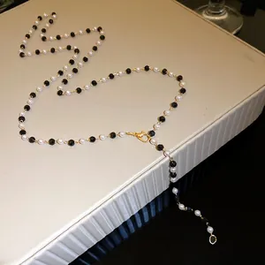 Close-up detail of a pearl and black bead necklace resting on a textured jewelry box