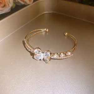 Detailed view of gold double-layered open bangle with zircon butterfly and pearl accents