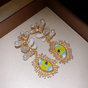Macro view of luxury gold earrings featuring pearls, rhinestones, and vibrant evil eye pendants.