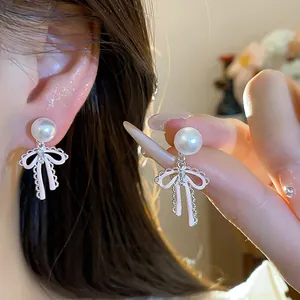 Close-up of pink enamel bow pearl earrings on model's ear and hand