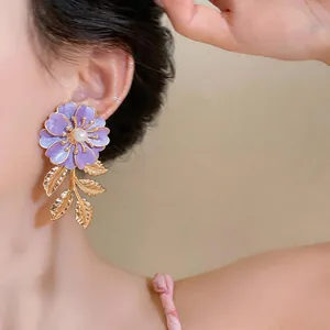 Nahaufnahme von lila Emaille-Blumenohrring mit weißer Perle und goldenen Blattquasten