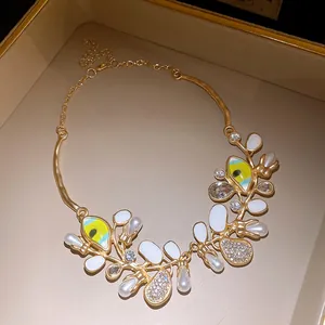 Close-up of gold-toned geometric necklace with pearls, rhinestones, and green enamel detail.