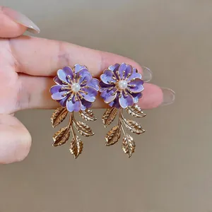 Detailansicht von lila Emaille-Blumenohrringen mit goldenen Blattquasten und Perlenmitte.