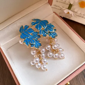 Close-up detail of blue enamel maple leaf earrings featuring white pearl grape clusters