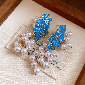 Detail of elegant grape earrings with blue enamel leaves and clustered white pearls.