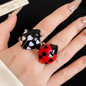 Red and black enamel ladybug open ring with heart patterns on hand model
