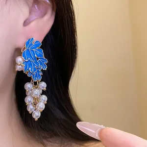 Detailed macro view of blue enamel leaf and pearl grape pendant earring worn on ear