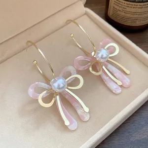 Sweet pink acetate bow drop earrings with pearls and gold hoops on a velvet tray