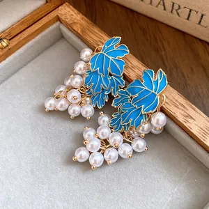 Detailed view of elegant blue enamel leaf earrings with clusters of white pearls.