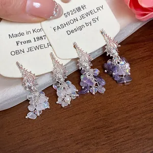 Macro view of conch-shaped tassel earrings featuring pearls and purple crystals for beach wear