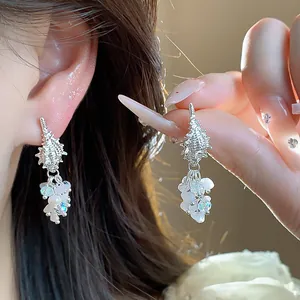 Close-up of silver conch tassel earrings with pearls and crystals for a seaside look.