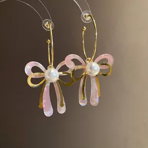 Detail of pink acetate bow earrings with pearls and golden hoops on warm background.
