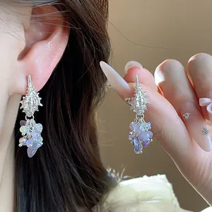 Detail shot of silver shell drop earrings featuring purple stone and crystal tassels.