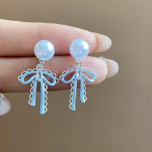 Detailed close-up of light blue enamel bow earrings featuring white pearl studs