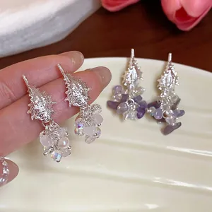 Detailed close-up of elegant silver conch shell earrings with crystal and pearl tassels