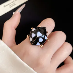 Detail view of a black enamel ladybug ring with white heart spots on a model's finger.