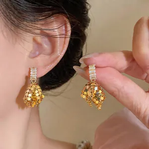 Detailed shot of French style gold earrings with baguette-cut zircons and textured charms