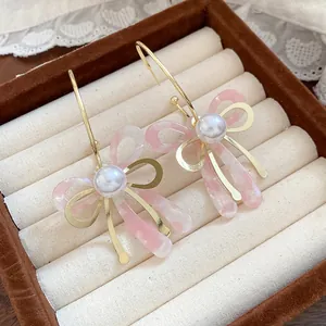 Detail of sweet pink acetate bow earrings with central pearl and gold hooks
